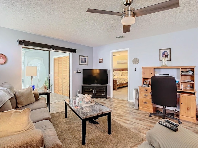 living room with ceiling fan, a textured ceiling, and light hardwood / wood-style flooring