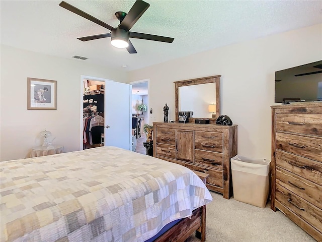 bedroom with ceiling fan, a spacious closet, light colored carpet, a textured ceiling, and a closet