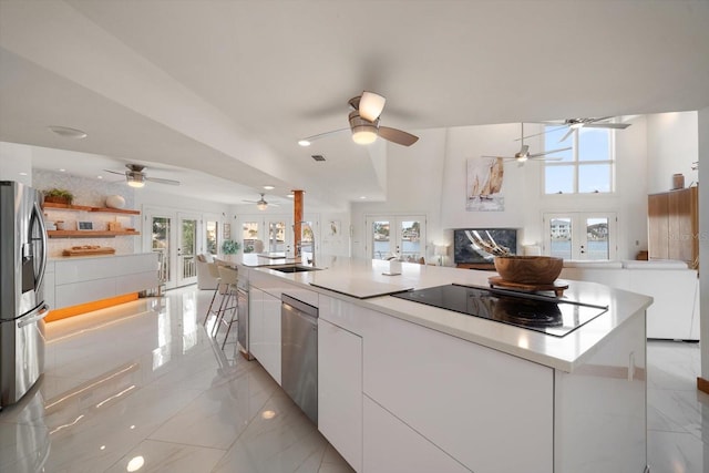 kitchen with a large island with sink, french doors, appliances with stainless steel finishes, a wealth of natural light, and white cabinetry