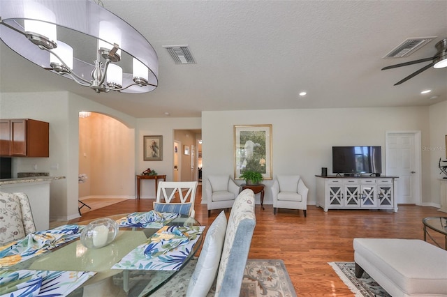 dining room with ceiling fan with notable chandelier, wood-type flooring, and a textured ceiling