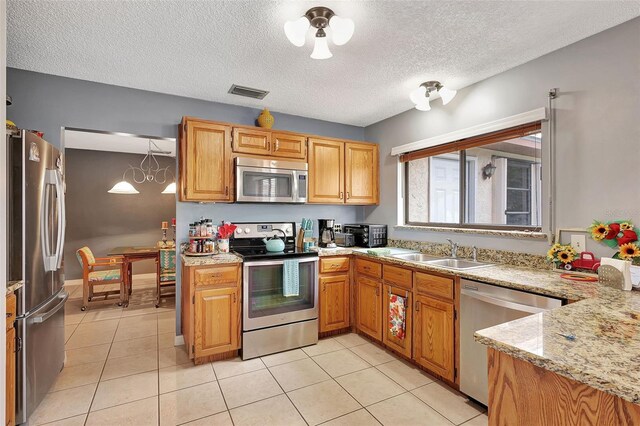 kitchen with appliances with stainless steel finishes, light stone counters, a textured ceiling, sink, and light tile patterned flooring