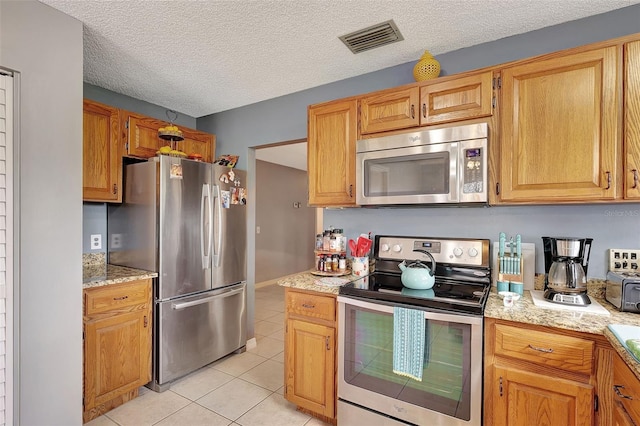 kitchen featuring light stone countertops, light tile patterned floors, a textured ceiling, and appliances with stainless steel finishes