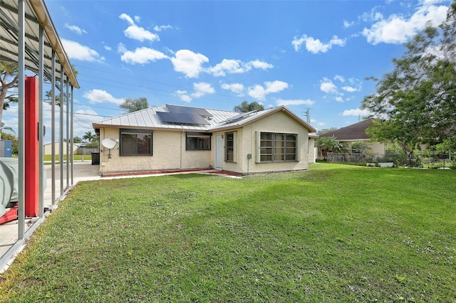 rear view of property featuring a lawn and solar panels