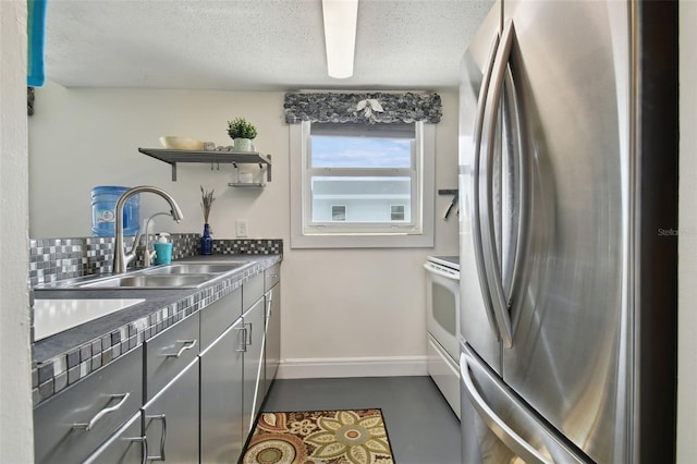 kitchen featuring white stove, sink, decorative backsplash, stainless steel fridge, and concrete floors