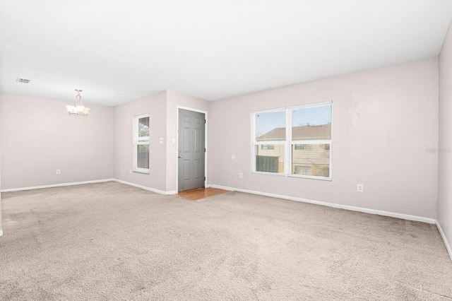 spare room featuring an inviting chandelier, baseboards, and carpet