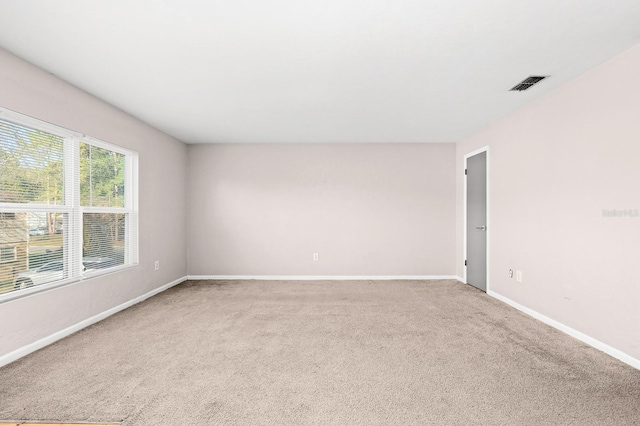 empty room with baseboards, visible vents, and light carpet