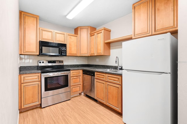 kitchen featuring a sink, dark countertops, tasteful backsplash, stainless steel appliances, and light wood-style floors