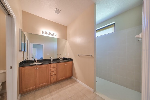 bathroom with vanity, tile patterned flooring, toilet, a textured ceiling, and a tile shower