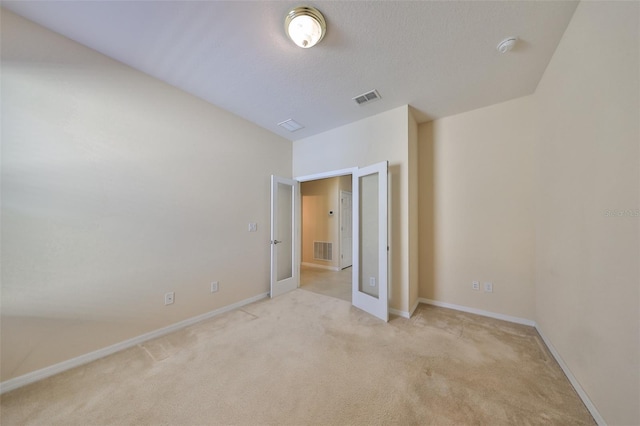 unfurnished bedroom with french doors, a textured ceiling, and light colored carpet