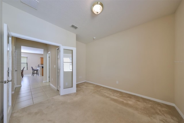 unfurnished room with light carpet, french doors, and a textured ceiling