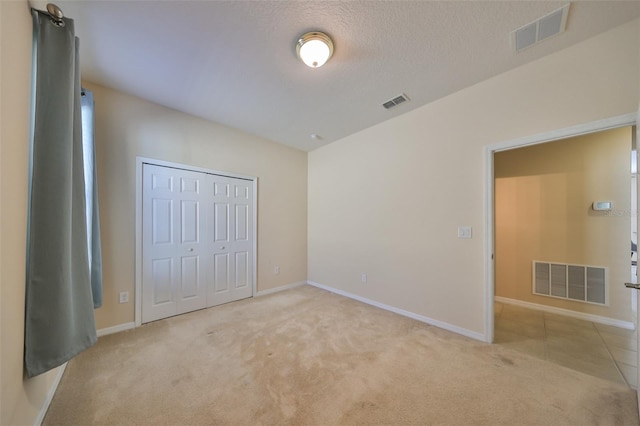 unfurnished bedroom featuring a textured ceiling, light colored carpet, and a closet