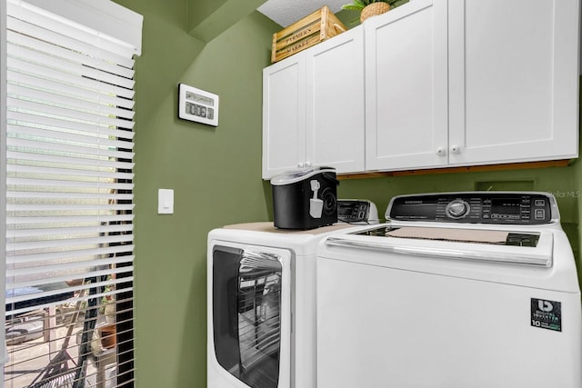 clothes washing area featuring washer and dryer, a healthy amount of sunlight, and cabinets