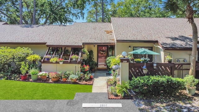 view of front of property featuring a shingled roof, a front yard, and stucco siding