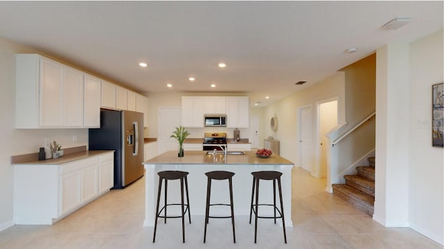 kitchen featuring white cabinets, appliances with stainless steel finishes, light tile patterned floors, and a kitchen island with sink