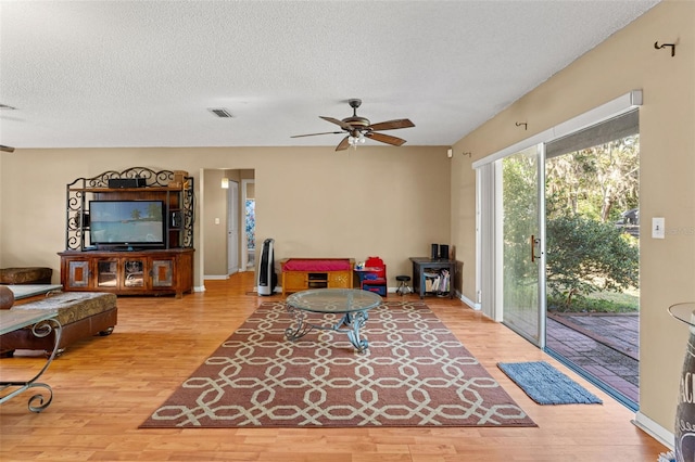 living room featuring hardwood / wood-style flooring, ceiling fan, and a textured ceiling