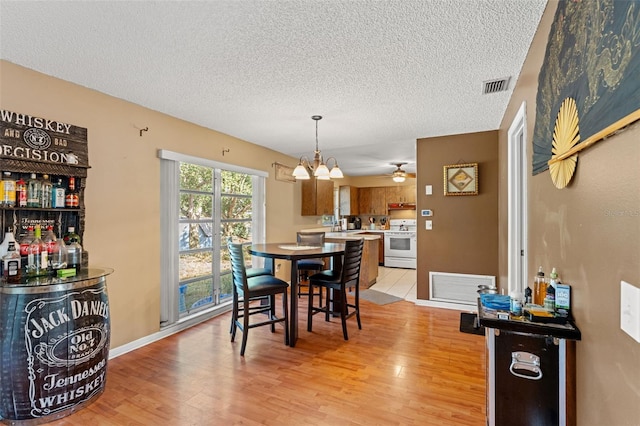 dining area featuring a textured ceiling, light hardwood / wood-style flooring, and ceiling fan with notable chandelier