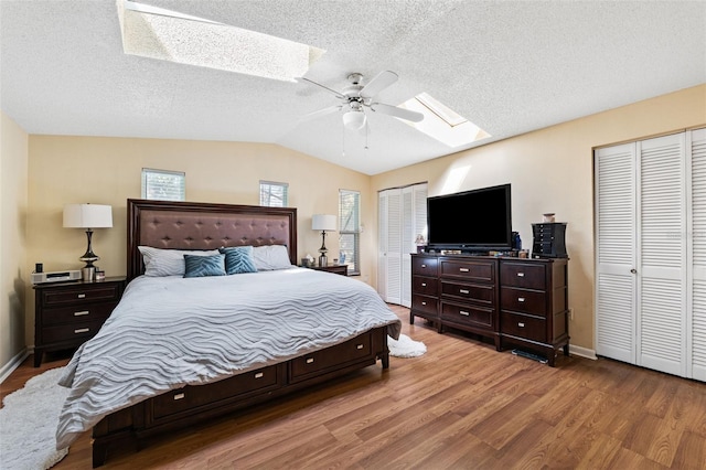 bedroom with a textured ceiling, lofted ceiling with skylight, ceiling fan, wood-type flooring, and multiple closets