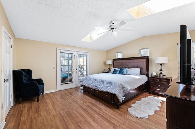 bedroom with access to exterior, ceiling fan, a textured ceiling, vaulted ceiling with skylight, and hardwood / wood-style flooring