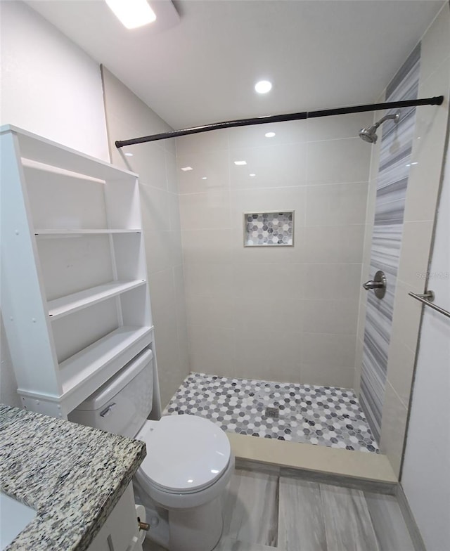 bathroom featuring a tile shower, vanity, and toilet