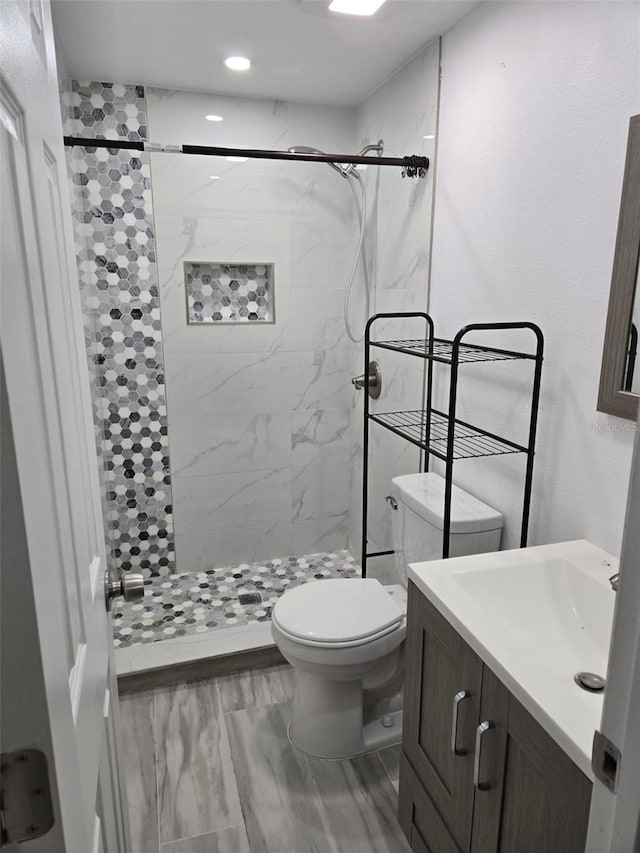 bathroom with a tile shower, vanity, and toilet