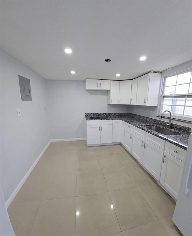 kitchen with light tile patterned flooring, dark stone countertops, white cabinetry, and sink