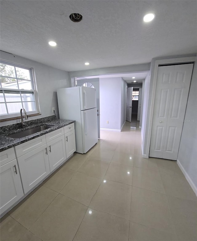 kitchen with white cabinets, sink, dark stone countertops, a textured ceiling, and white fridge