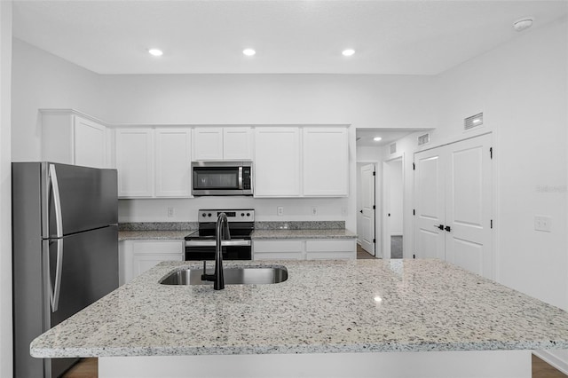 kitchen with light stone counters, stainless steel appliances, sink, white cabinets, and an island with sink