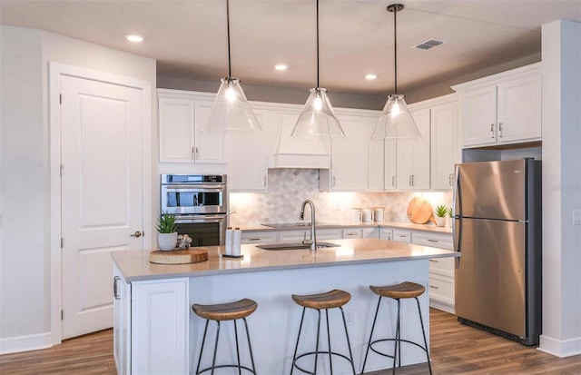 kitchen with dark wood-type flooring, stainless steel appliances, white cabinetry, and a center island with sink