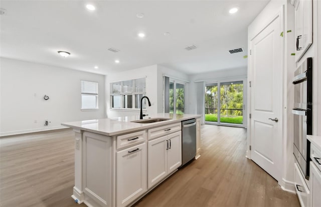 kitchen featuring white cabinetry, an island with sink, sink, stainless steel appliances, and light hardwood / wood-style flooring