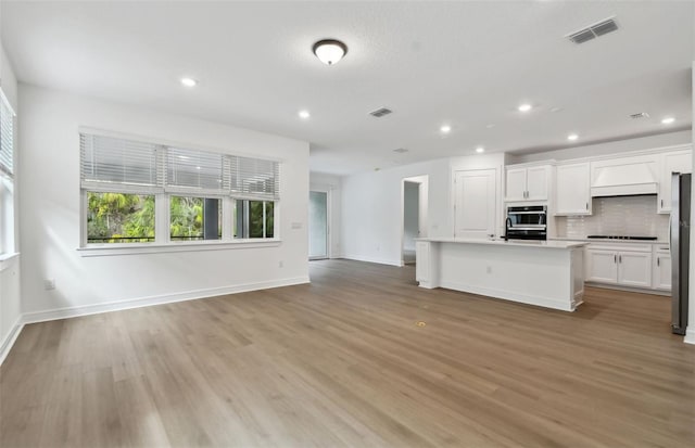 kitchen with tasteful backsplash, white cabinetry, a kitchen island with sink, and light hardwood / wood-style floors