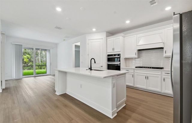 kitchen featuring an island with sink, sink, white cabinets, decorative backsplash, and black appliances