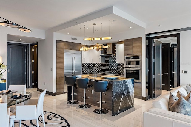 kitchen with a breakfast bar, stainless steel appliances, wall chimney range hood, a center island, and hanging light fixtures