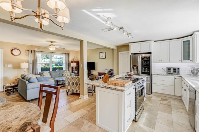 kitchen featuring white cabinetry, hanging light fixtures, light stone counters, decorative backsplash, and appliances with stainless steel finishes