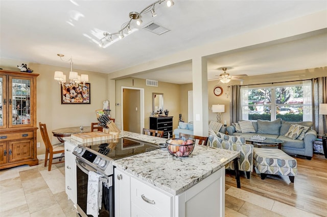 kitchen with stainless steel range with electric stovetop, pendant lighting, white cabinets, ceiling fan with notable chandelier, and light hardwood / wood-style floors