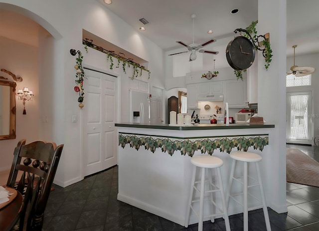 kitchen with kitchen peninsula, ceiling fan, white fridge with ice dispenser, white cabinetry, and a breakfast bar area