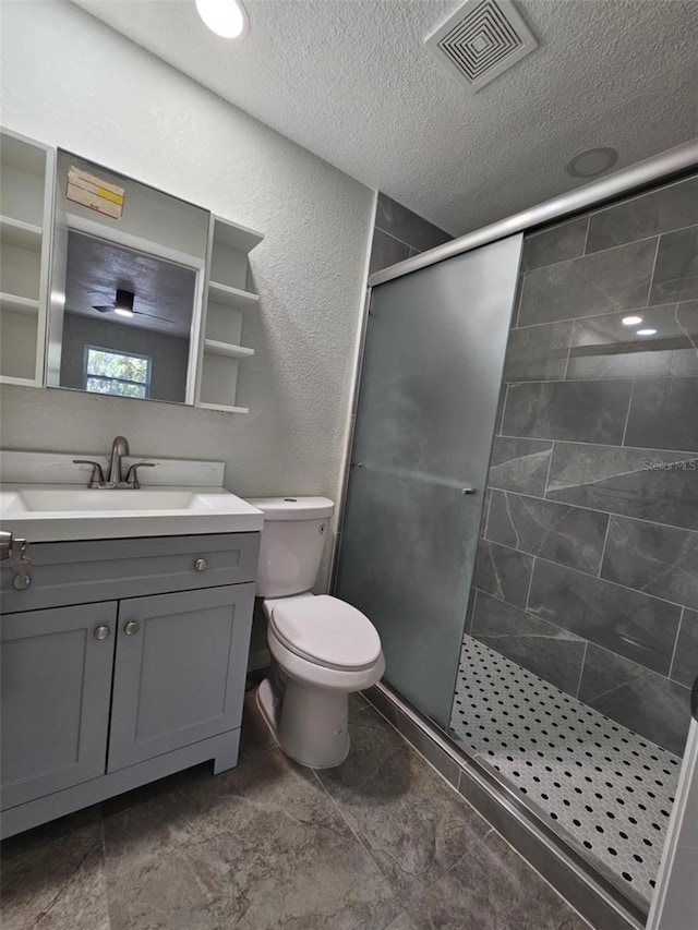 bathroom featuring vanity, toilet, a shower with shower door, and a textured ceiling