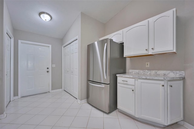 kitchen with stainless steel fridge, vaulted ceiling, white cabinetry, and light tile patterned floors