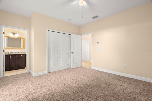 unfurnished bedroom with ensuite bath, ceiling fan, sink, light colored carpet, and a closet