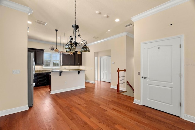 kitchen featuring a center island, pendant lighting, wood-type flooring, a breakfast bar, and ornamental molding