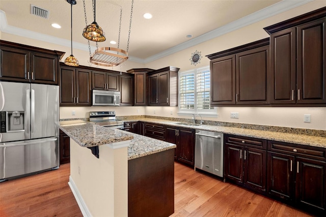 kitchen with decorative light fixtures, a center island, stainless steel appliances, and light hardwood / wood-style flooring