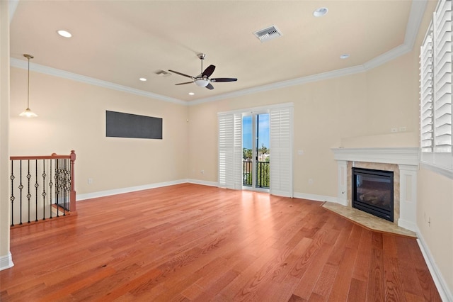 unfurnished living room featuring plenty of natural light, a tiled fireplace, crown molding, and light hardwood / wood-style flooring