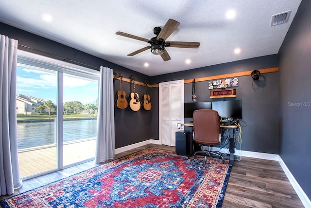 office area with a textured ceiling, dark hardwood / wood-style floors, ceiling fan, and a water view