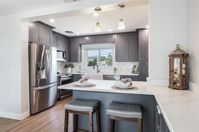 kitchen featuring pendant lighting, light hardwood / wood-style flooring, decorative backsplash, a kitchen bar, and stainless steel appliances