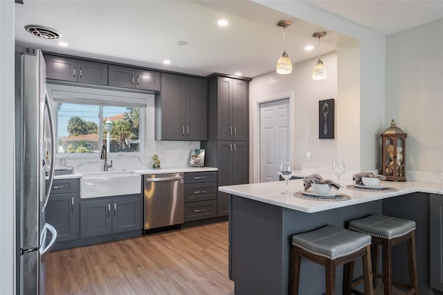 kitchen with kitchen peninsula, appliances with stainless steel finishes, a kitchen bar, sink, and decorative light fixtures