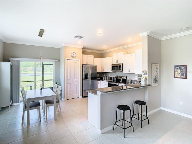 kitchen featuring kitchen peninsula, dark stone countertops, ornamental molding, appliances with stainless steel finishes, and white cabinetry