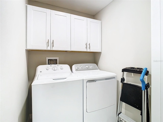 clothes washing area with separate washer and dryer and cabinets