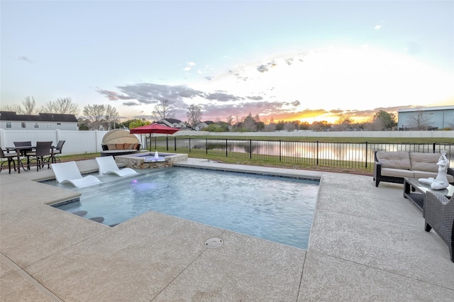 pool at dusk featuring a patio area, a water view, and an in ground hot tub