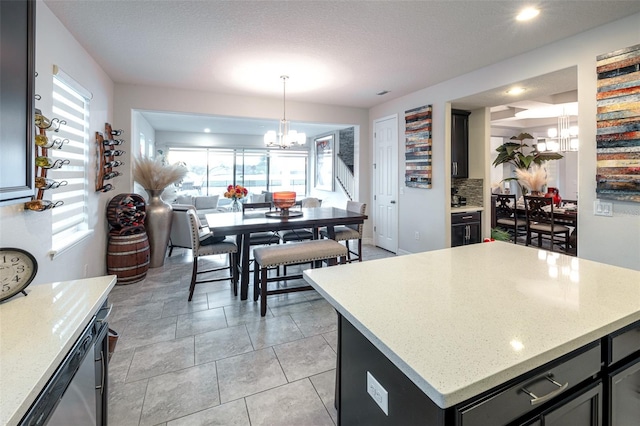 kitchen with decorative backsplash, a textured ceiling, decorative light fixtures, a kitchen island, and a chandelier