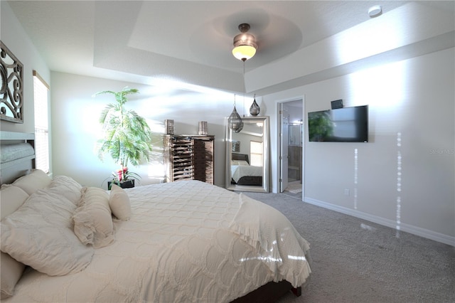 bedroom featuring carpet, ensuite bathroom, a raised ceiling, and ceiling fan