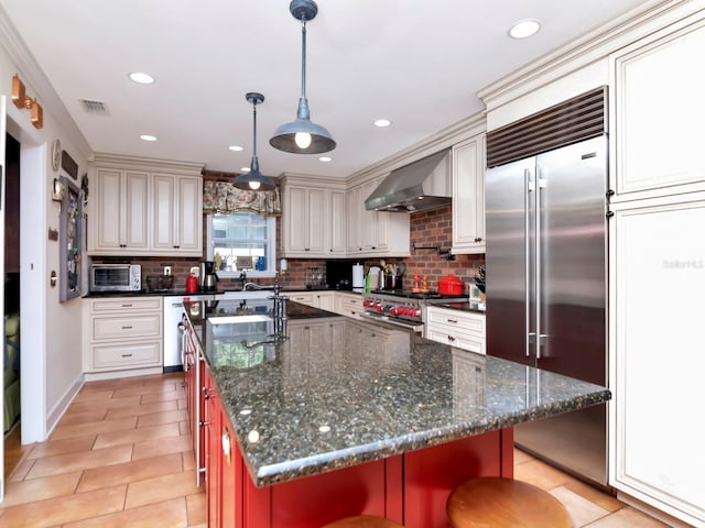 kitchen with wall chimney range hood, backsplash, a kitchen bar, a center island with sink, and high end appliances